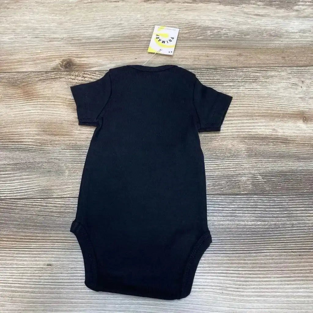 Flat lay back view of black organic newborn bodysuit showcasing ribbed knit and short sleeves with attached tag on wood background