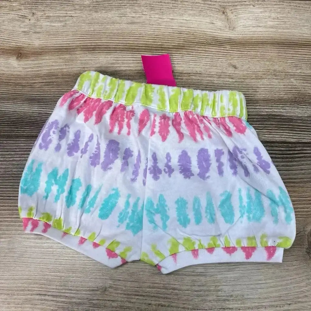 Top-down view of white baby pull-on shorts with multicolor tie-dye (3M), elastic waistband and gathered leg openings on wood background