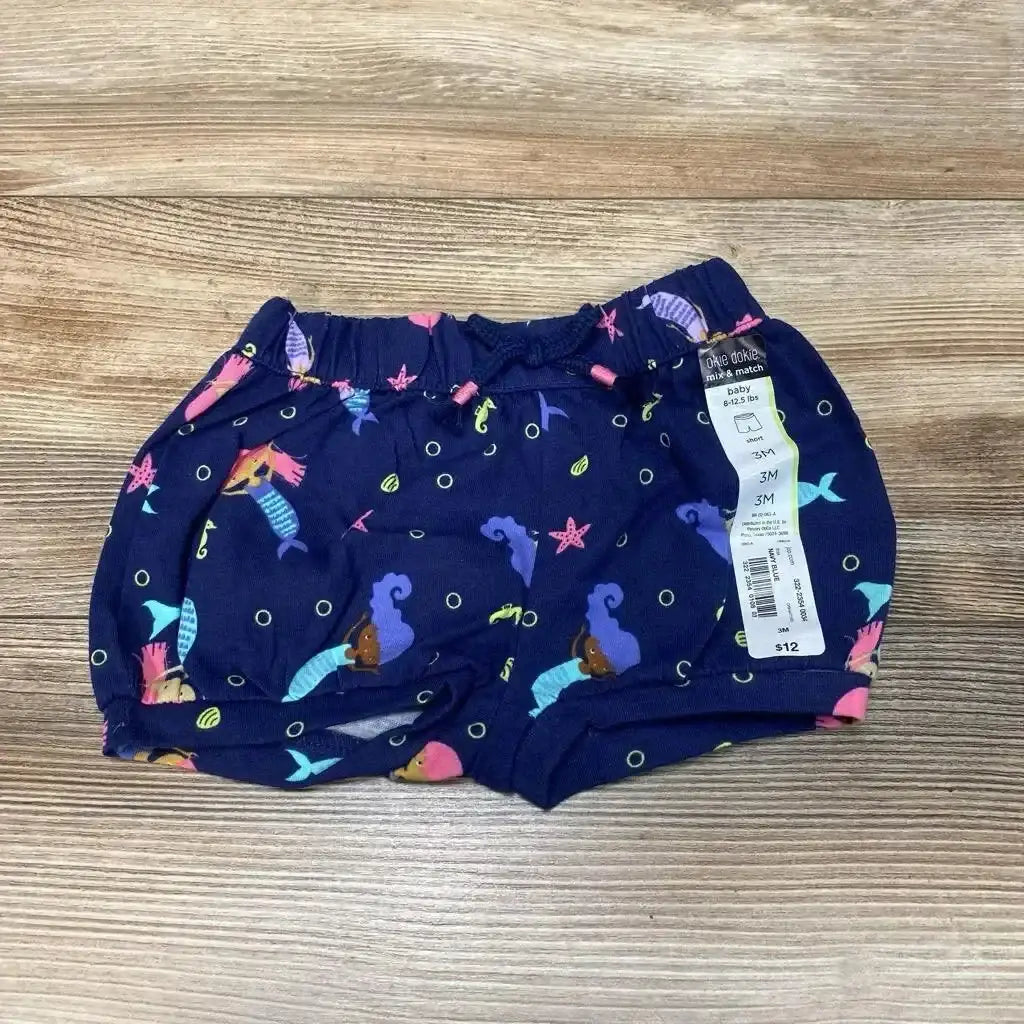 Top-down view of navy mermaid bubble shorts size 3M showing elastic waistband, bubble leg cuffs, and mermaid print on wood background