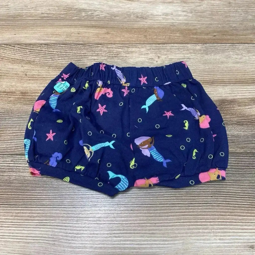 Top-down view of navy baby bubble shorts (3M) showing mermaid print, elastic waistband and gathered legs on wood surface