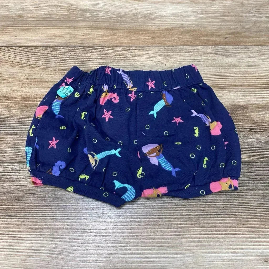 Top-down view of navy baby bubble shorts (3M) showing mermaid print, elastic waistband and gathered legs on wood surface