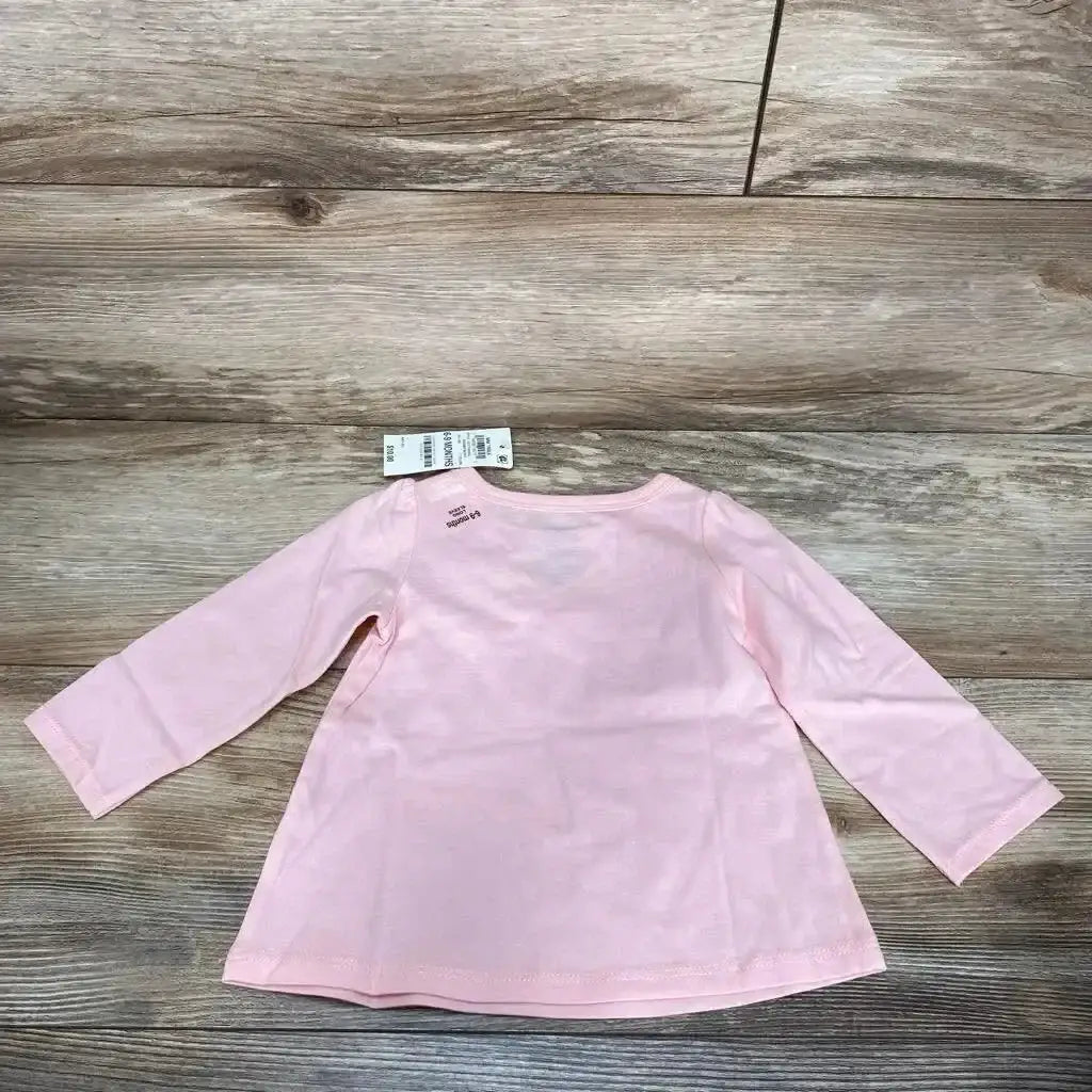 Back view of pink long-sleeve First Impressions baby shirt (6-9 months) showing A-line hem and size tag on wood