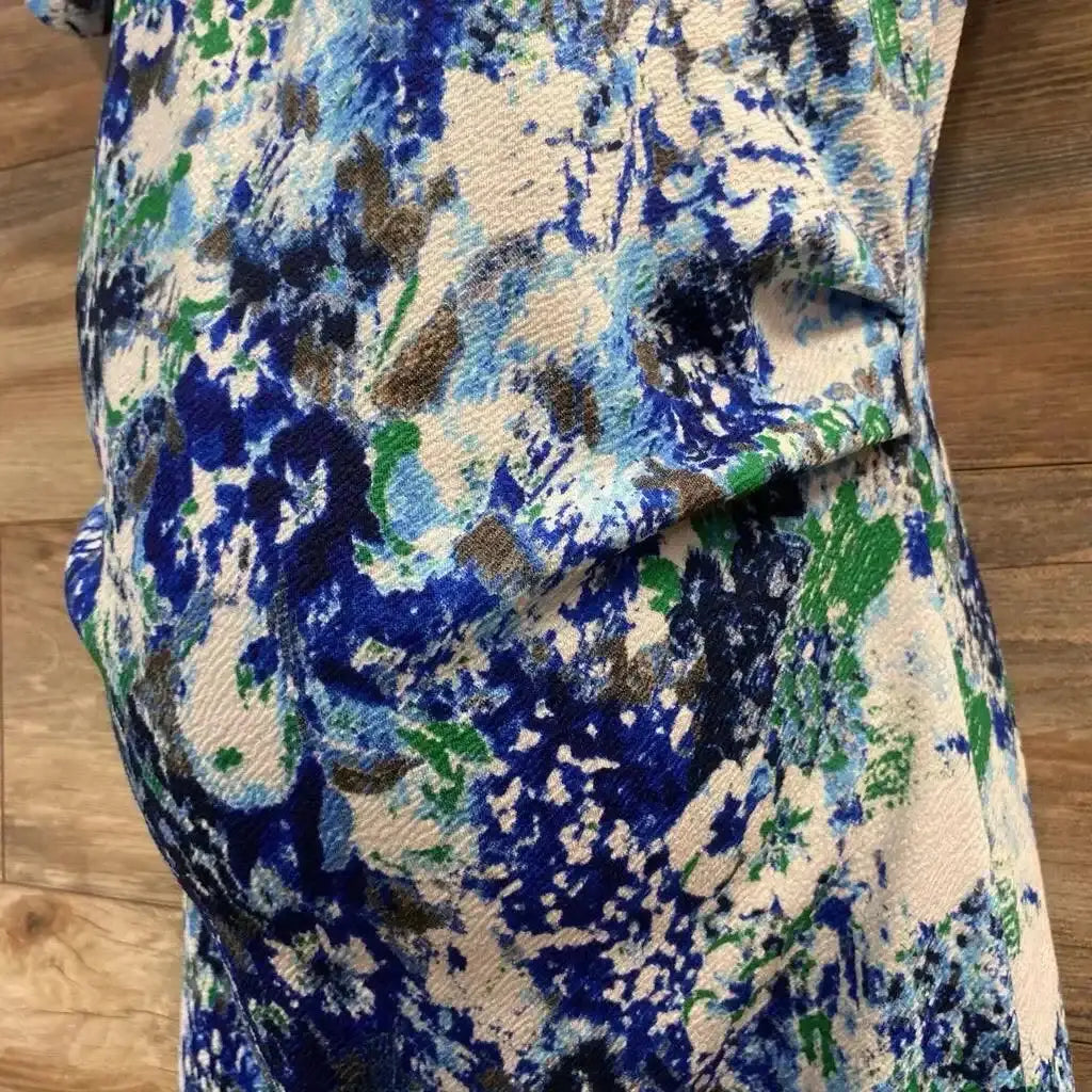 Close-up side view of maternity bodycon dress showing blue, green and navy floral print and fitted belly on wood floor