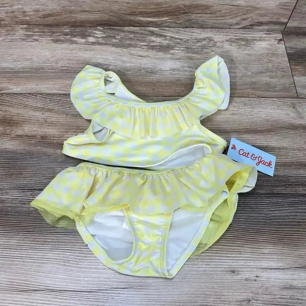 Top-down view of toddler yellow gingham 2-piece bikini set showing ruffle off-shoulder top and skirted bottoms on wood floor background