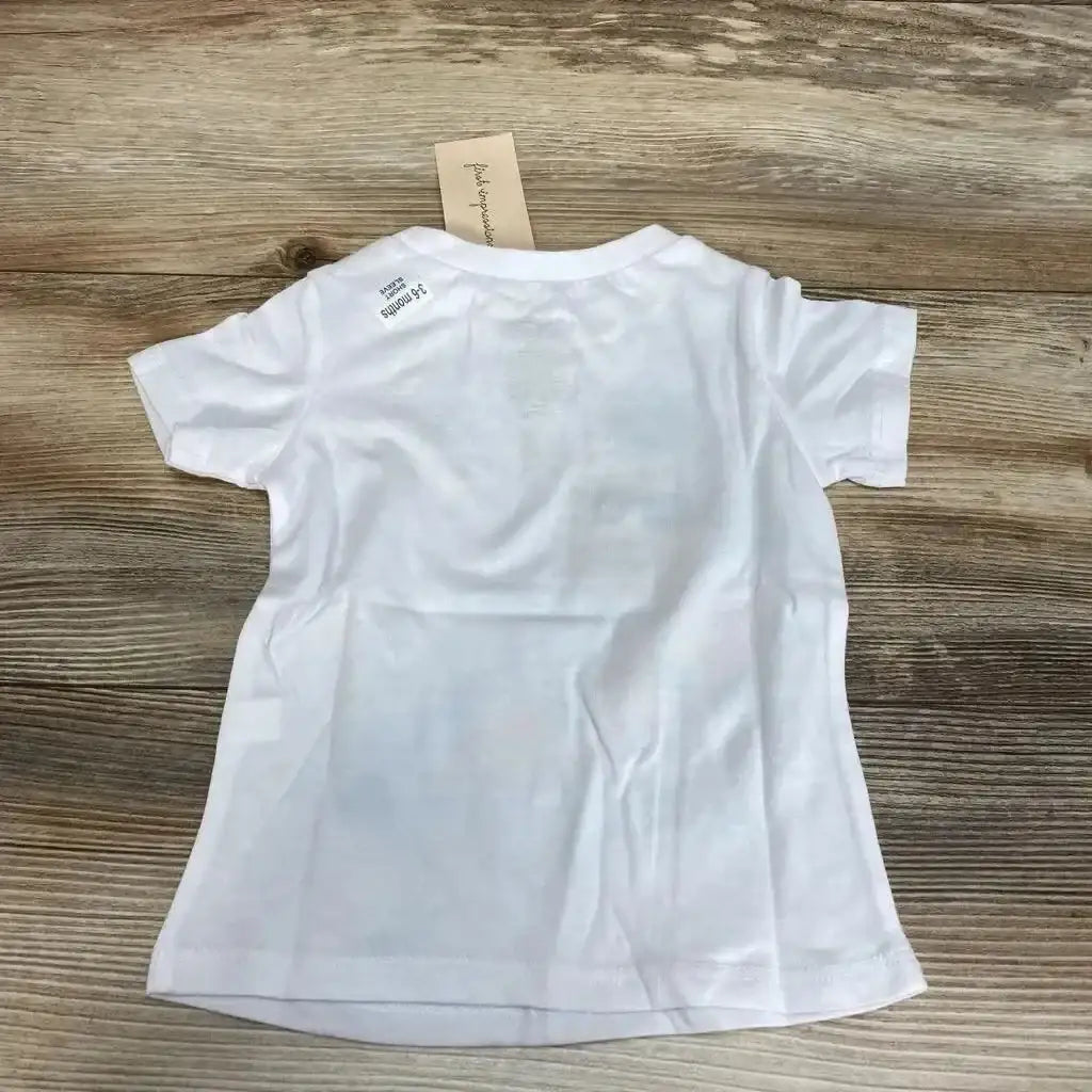 Back view of white First Impressions baby t-shirt (3-6 months) showing short sleeves, size sticker and hang tag on wood background