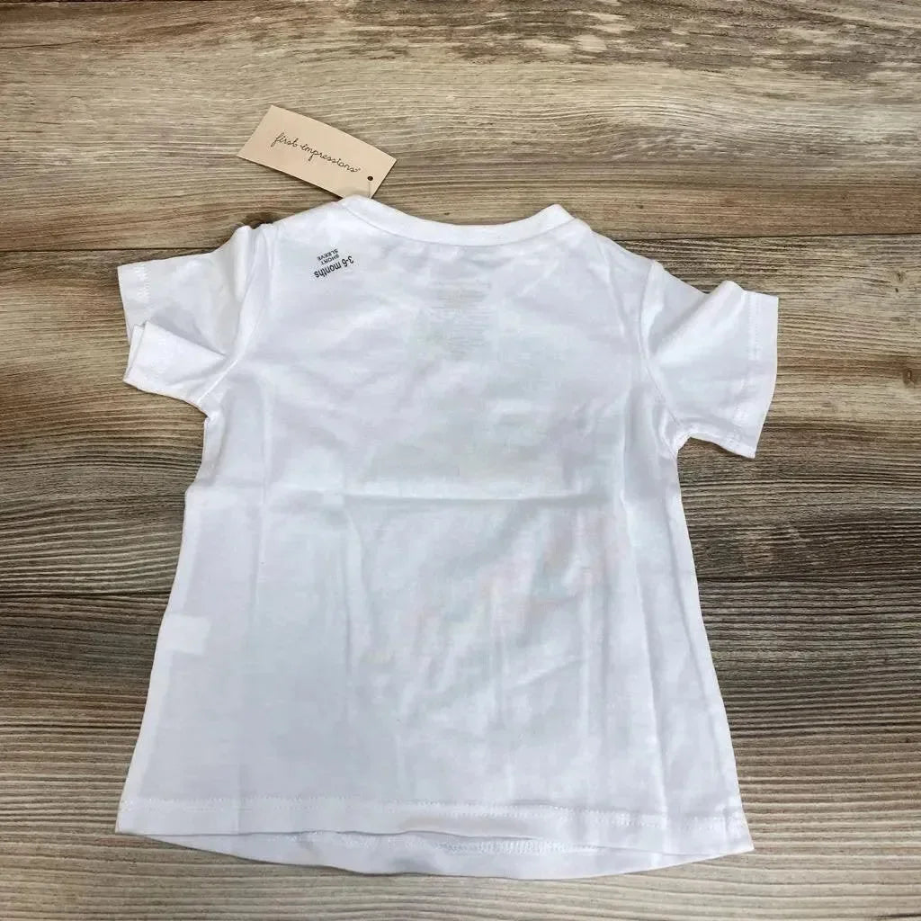Back view of white First Impressions baby t-shirt (3-6 months) showing short sleeves and attached tag on wood background