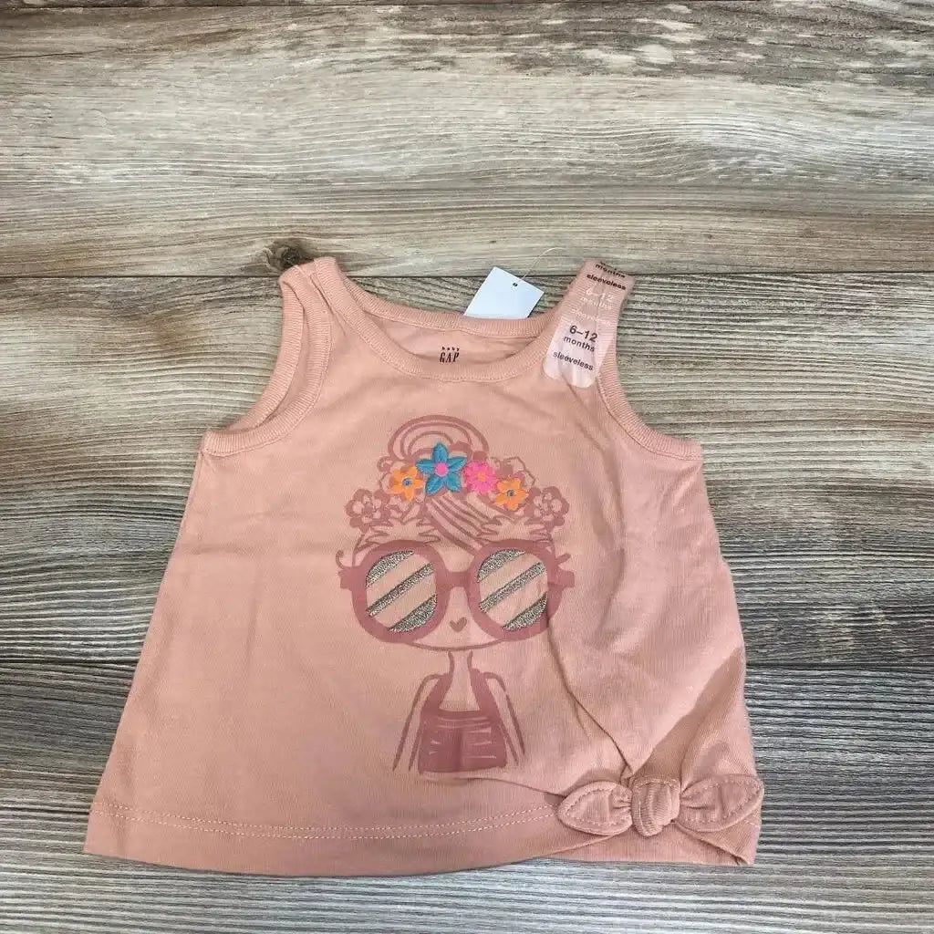 Flat-lay of pink Baby Gap tank top (6–12 months) showcasing front-tie knot and embroidered girl graphic with glitter-striped sunglasses on wood surface