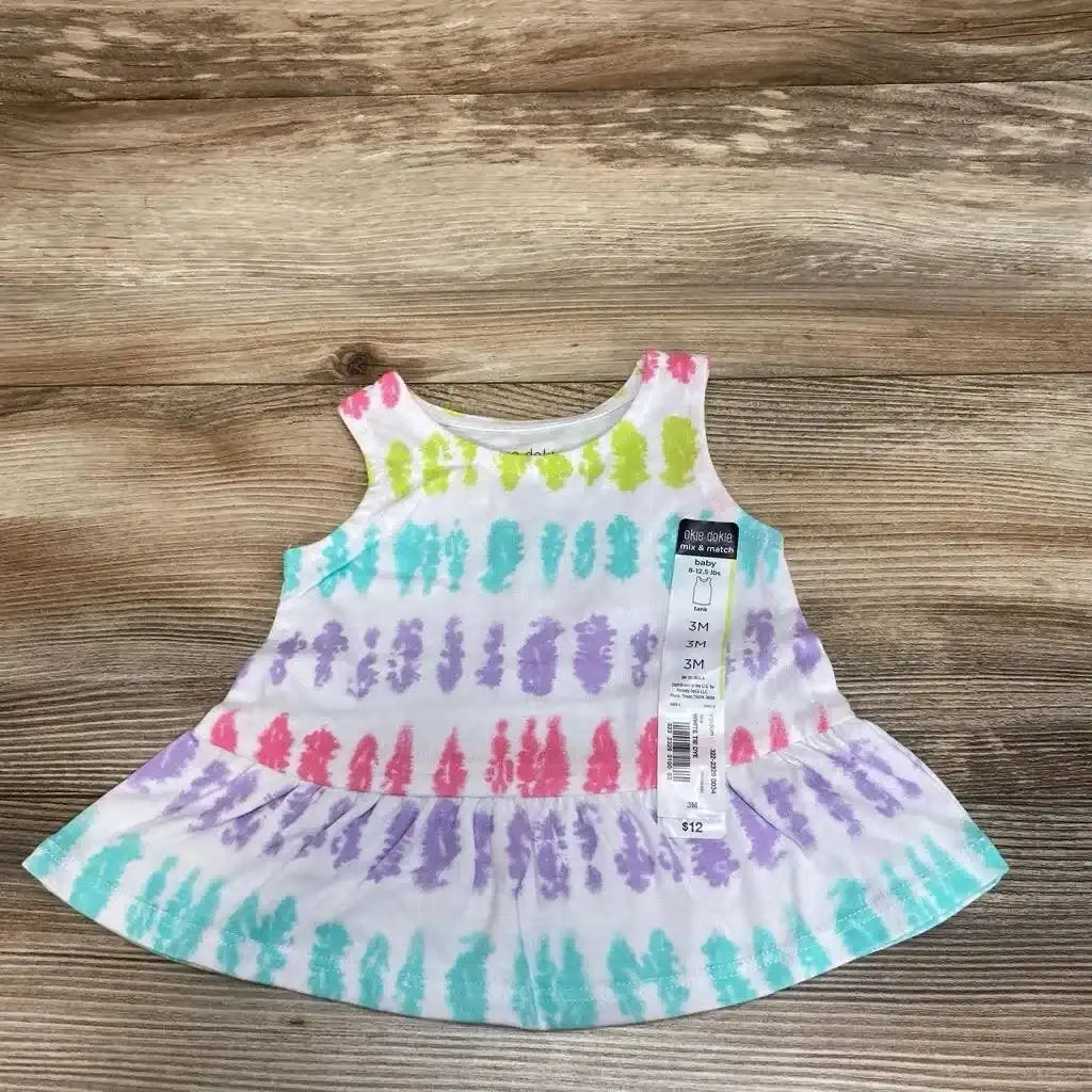 Flat lay of Okie Dokie white tank top with pink green teal and purple tie-dye stripes and hangtag on wood plank background