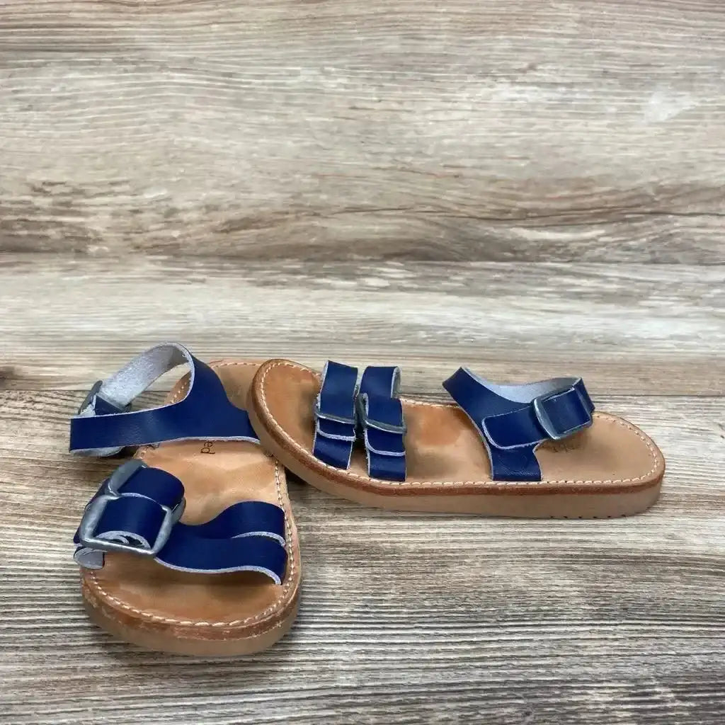 Angled overhead of navy Freshly Picked Rockaway sandals with double front straps, ankle buckle and tan stitched sole on wood