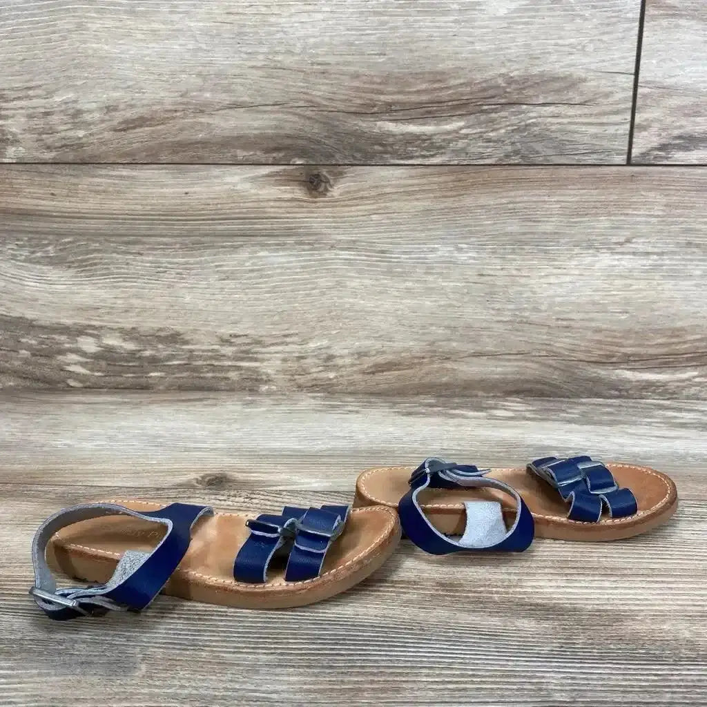 Side view of Freshly Picked Rockaway sandals size 8C showcasing double front straps with bow detail and ankle buckle on wood plank background