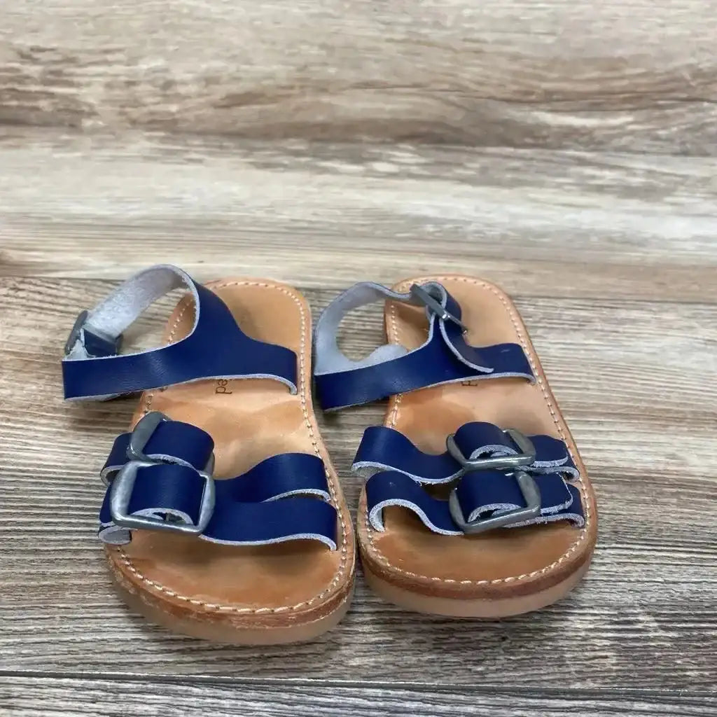 Top view of Freshly Picked Rockaway navy leather sandals with buckle straps and tan footbed on wood plank background