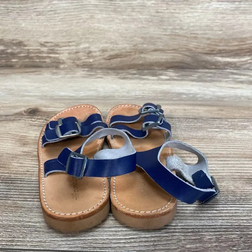 Angled overhead view of Freshly Picked Rockaway toddler sandals showing navy leather double-buckle straps and tan leather soles on wood background