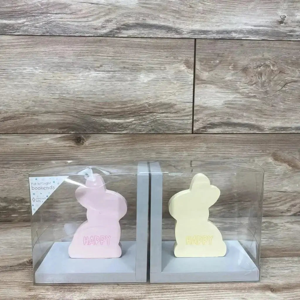 Front view of pink and yellow bunny bookends with HAPPY text on gray L shaped bases in clear packaging on wood background