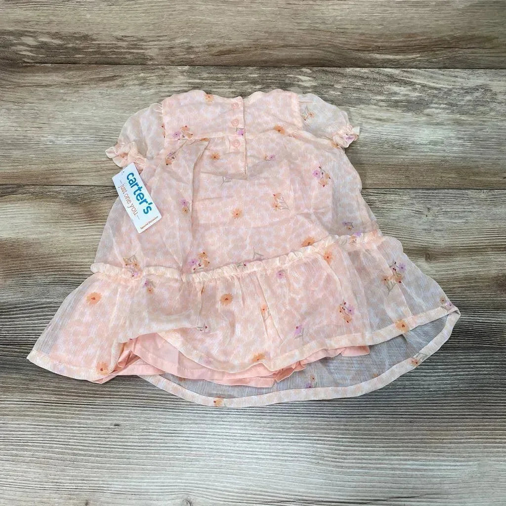 Flat lay of pink floral baby dress and matching bloomers with ruffled tier and sheer overlay on wood background