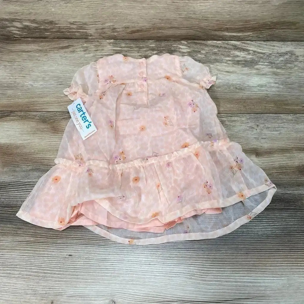 Flat lay of pink floral baby dress and matching bloomers with ruffled tier and sheer overlay on wood background