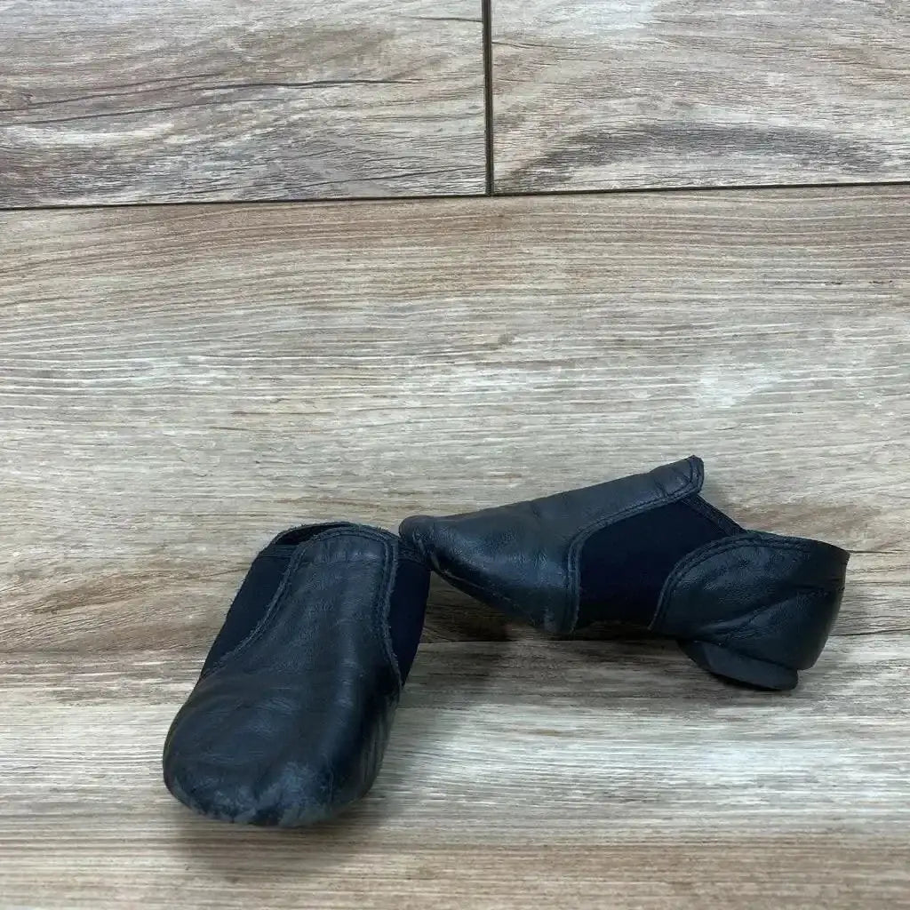 Three-quarter side view of black Capezio E-Series jazz slip-on shoes size 11C showcasing elastic gore and split sole on white background