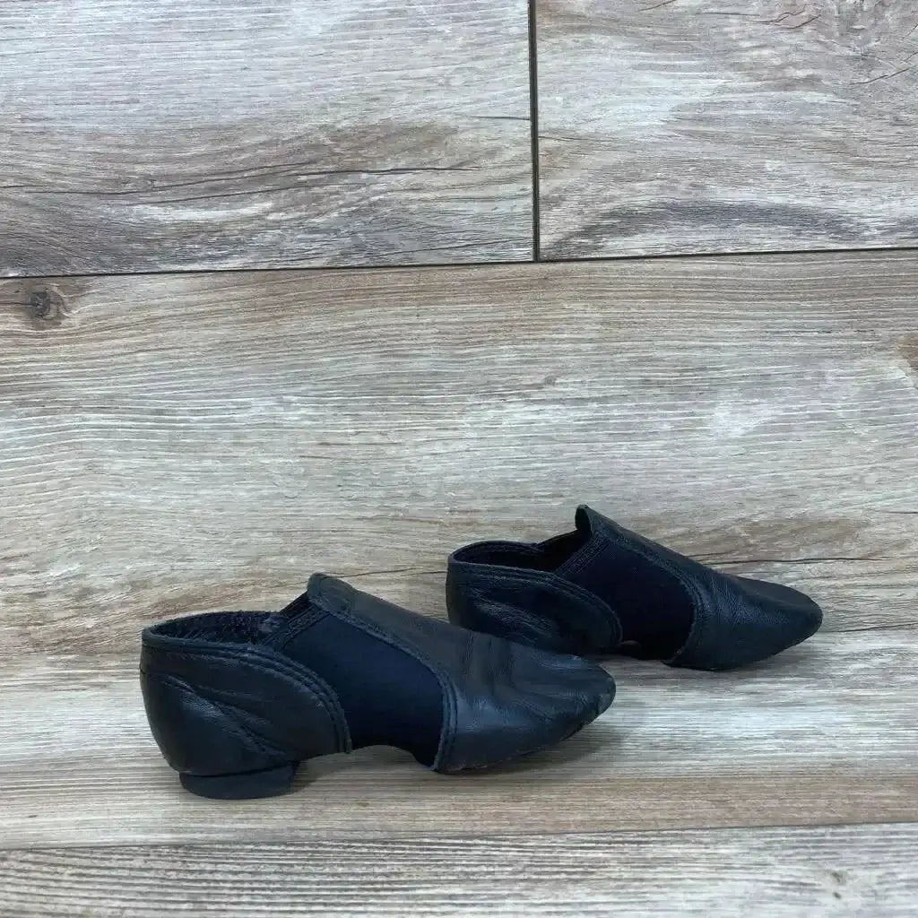 Side view of Capezio E-Series Jazz Slip-On Shoes sz 11c showcasing black leather pair with elastic gore on wood plank background