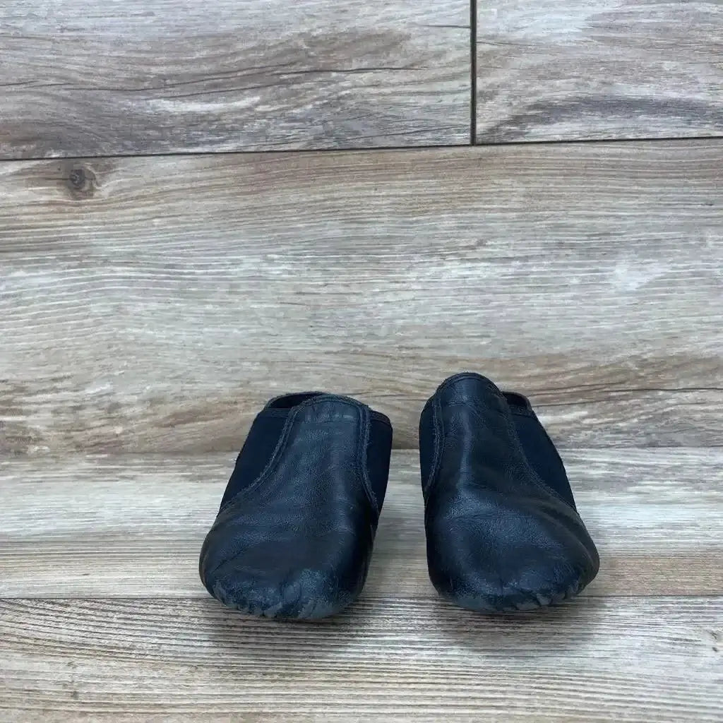 Front view of black Capezio E‑Series jazz slip-on shoes, size 11C, pair showing scuffed toes and elastic side panels on light wood floor