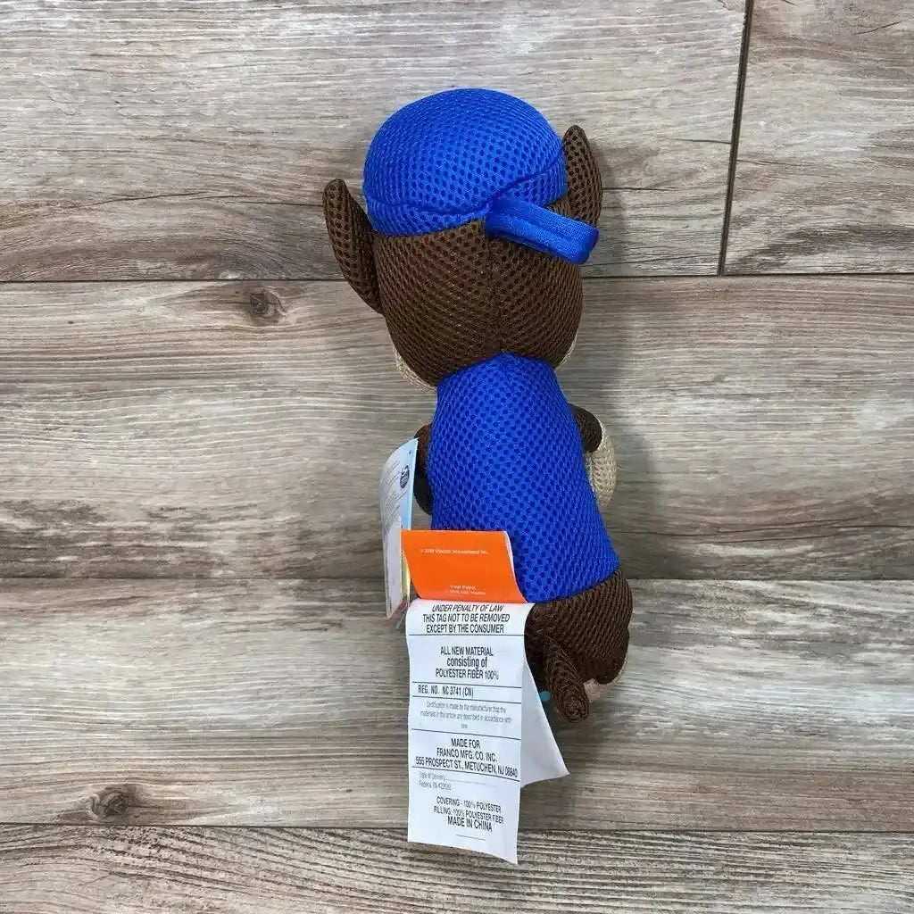 Back view of Paw Patrol plush toy showing blue mesh hat and vest with attached product tags on wood floor