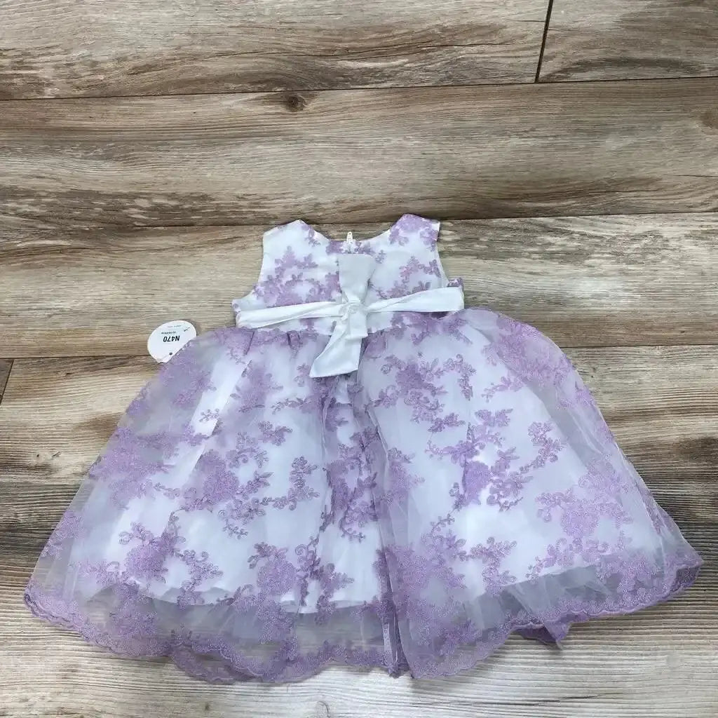 Top down view of white toddler dress 2T with lavender floral embroidery, satin waist bow and scalloped hem on wood floor