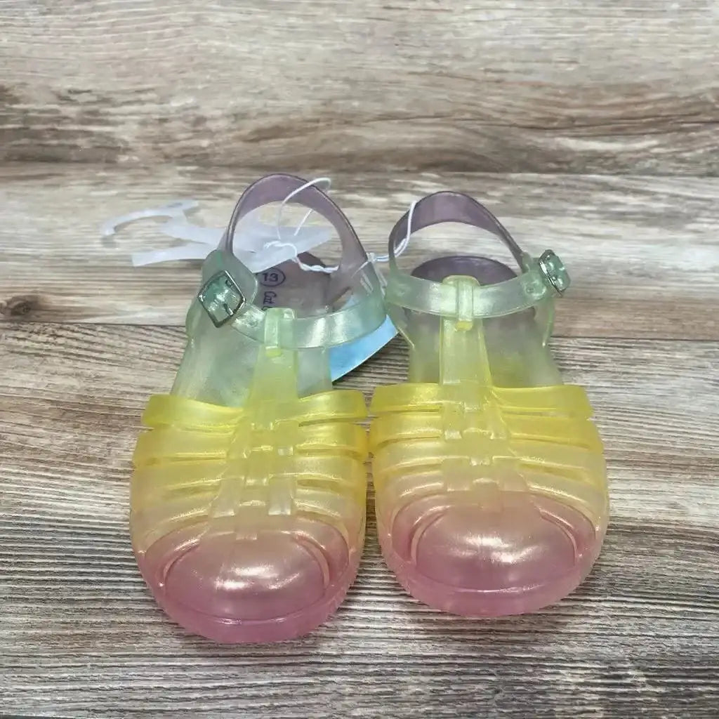 Front view of Cat & Jack jelly sandals size 13C showing translucent yellow-to-pink ombre, strappy toe and ankle buckle on wood