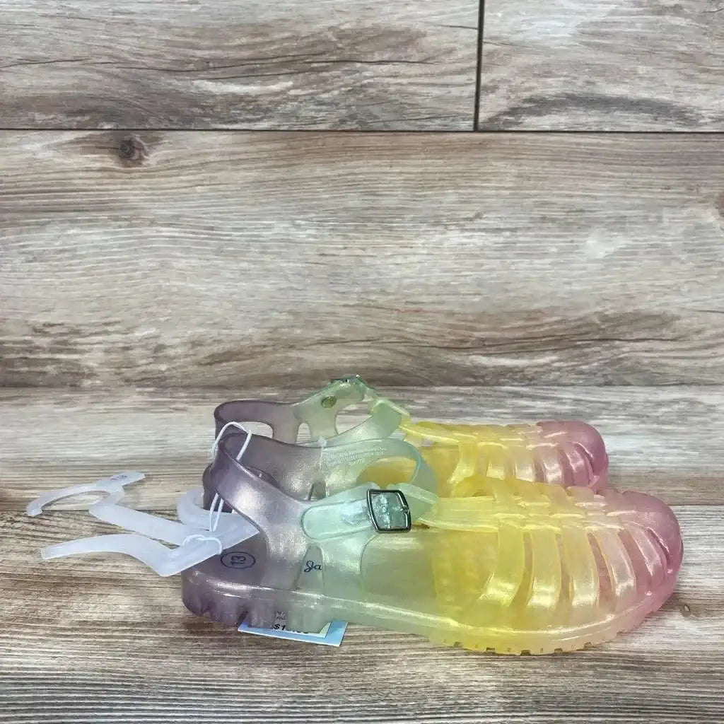 Side view of Cat & Jack jelly sandals, size 13C, translucent yellow-to-pink gradient with buckled ankle strap on wood