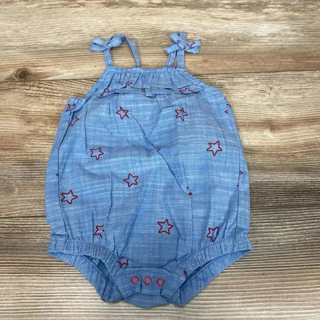 Flat lay of blue chambray romper (0-3M) with red star embroidery, tie straps, ruffle top and snap crotch on wood