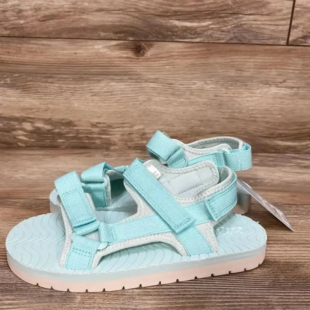 Side view of turquoise Cat and Jack toddler sandals with two Velcro straps, ridged footbed, and white sole on wood background
