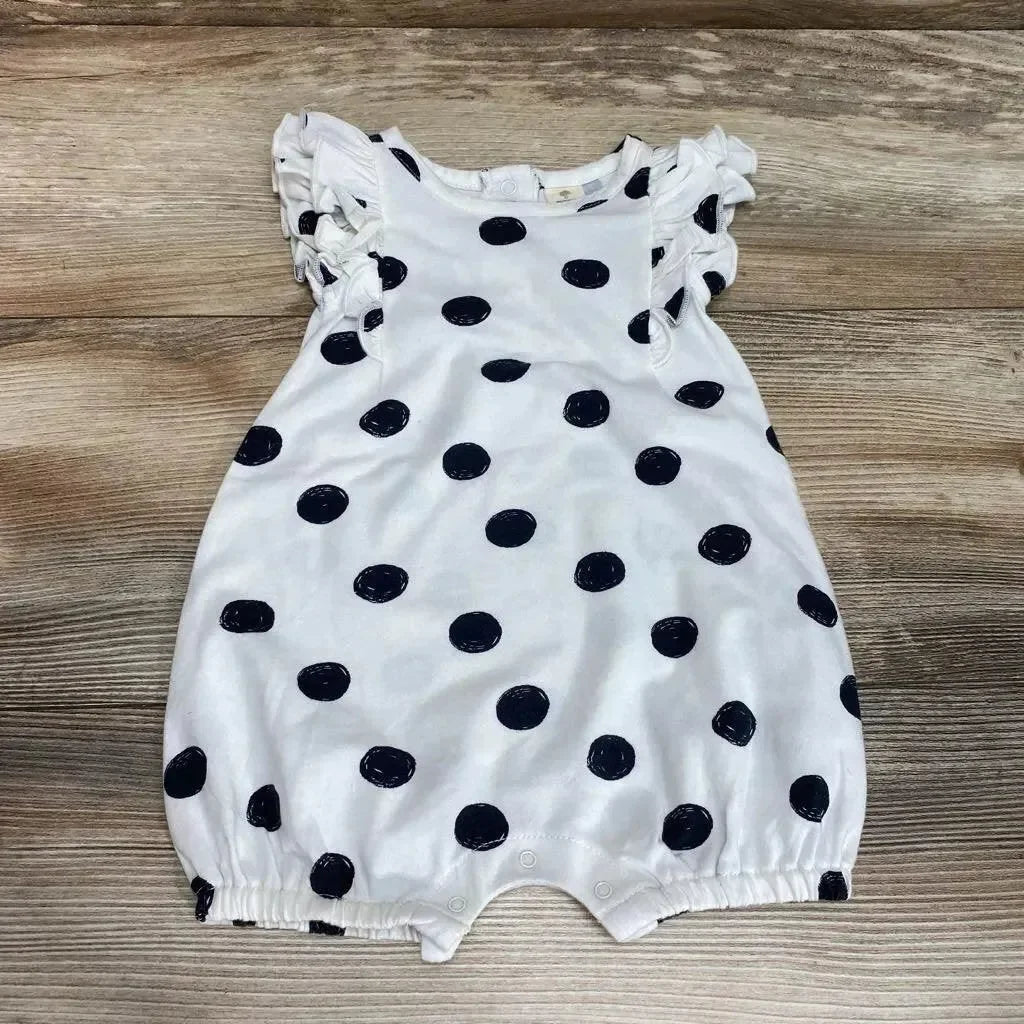 Flat lay of white polka-dot shortie romper with ruffle sleeves, snap crotch, and elastic leg openings on wooden floor