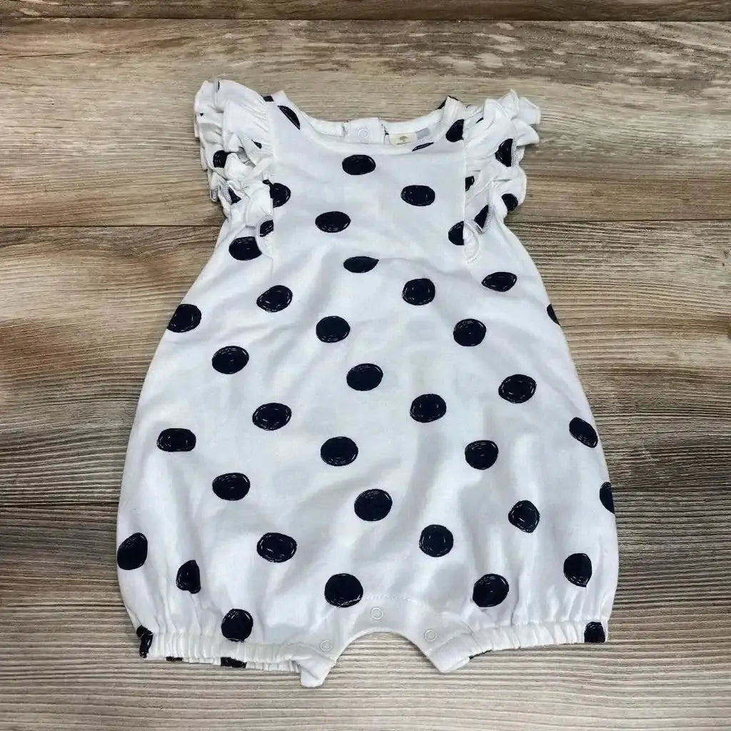 Flat lay of white polka-dot shortie romper with ruffle sleeves, snap crotch, and elastic leg openings on wooden floor