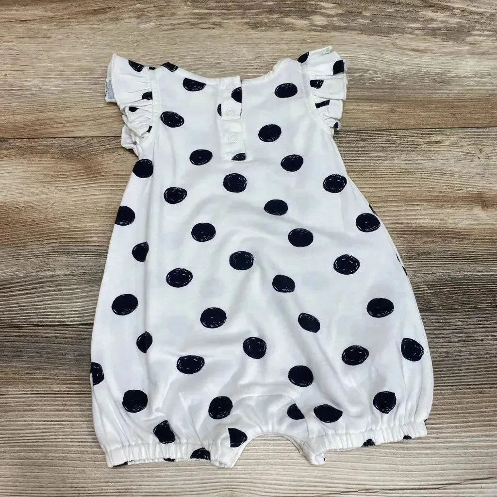 Flat lay of white baby romper with black polka dots, ruffle cap sleeves and elastic leg openings on wood background