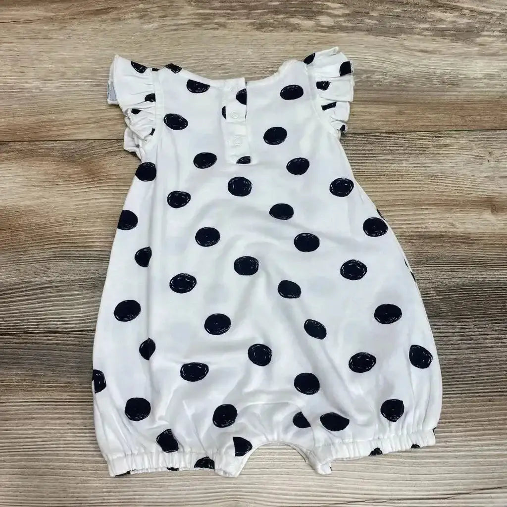 Flat lay of white baby romper with black polka dots, ruffle cap sleeves and elastic leg openings on wood background