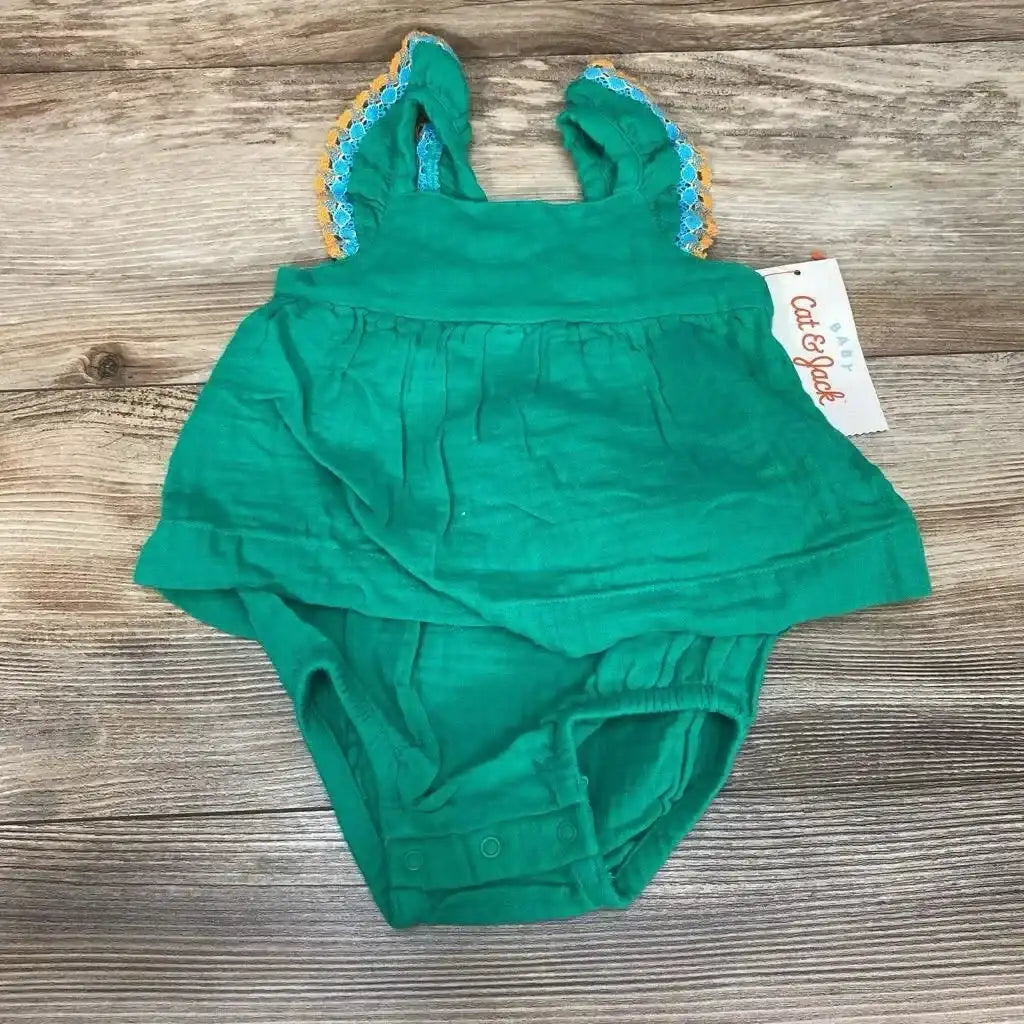 Top-down view of green muslin bodysuit dress showcasing ruffled lace-trim shoulder straps and snap crotch on wood background