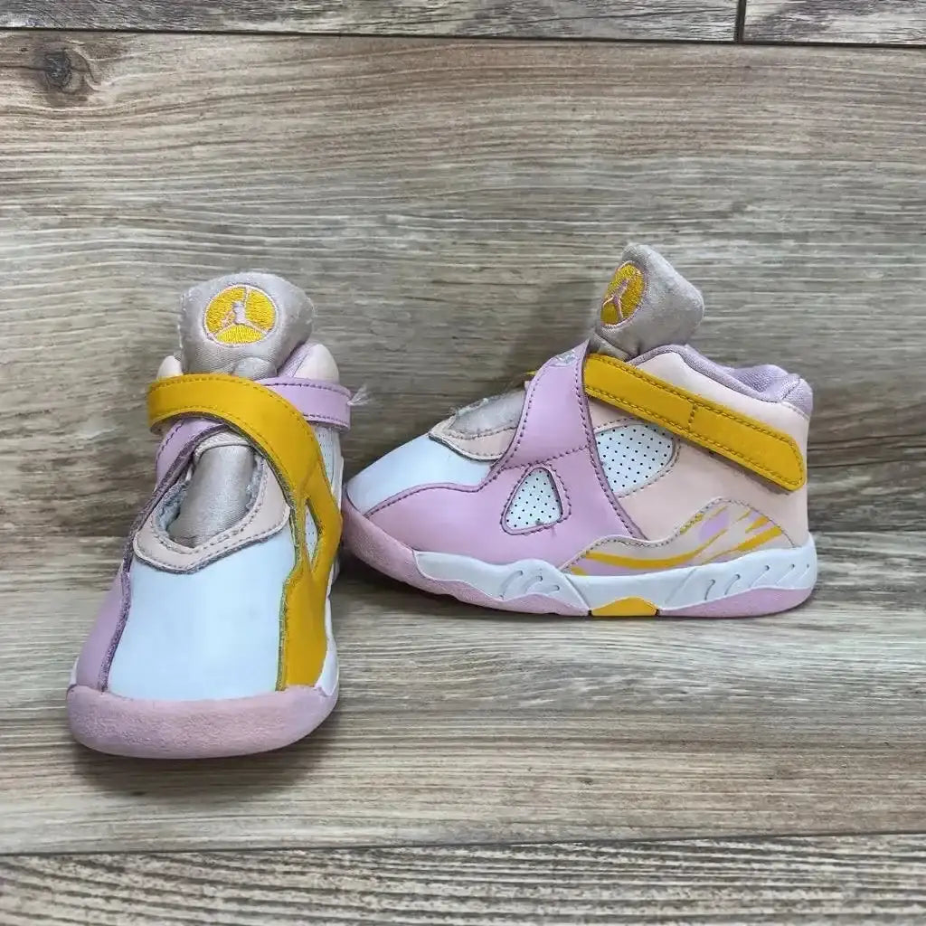 Side view of Air Jordan 8 Retro GS Arctic Punch sneakers showcasing pink white and yellow colorway with Jumpman tongue logo on wood plank background