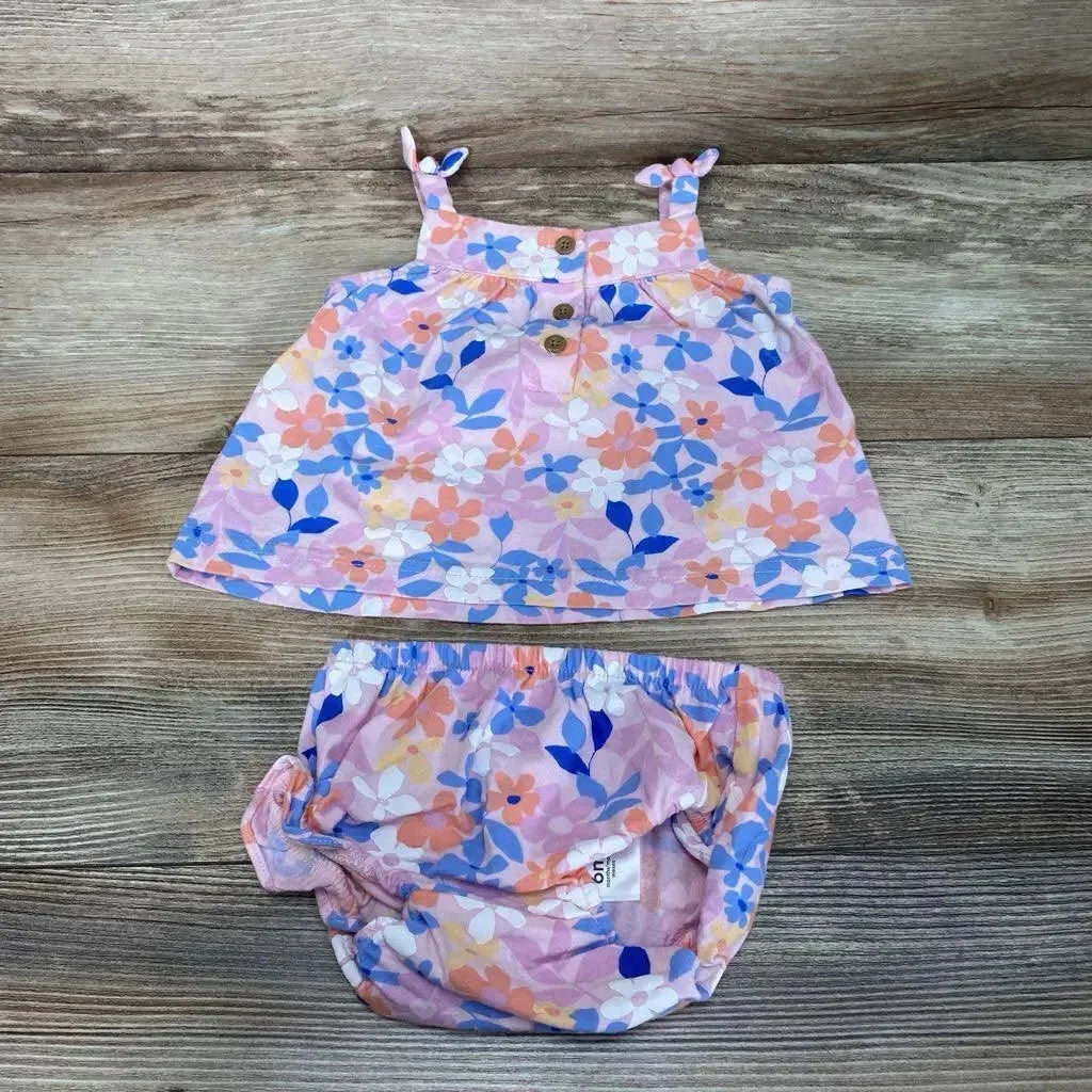 Flat lay of pink floral baby top with wooden-button straps and matching elastic-waist bloomers on wood background