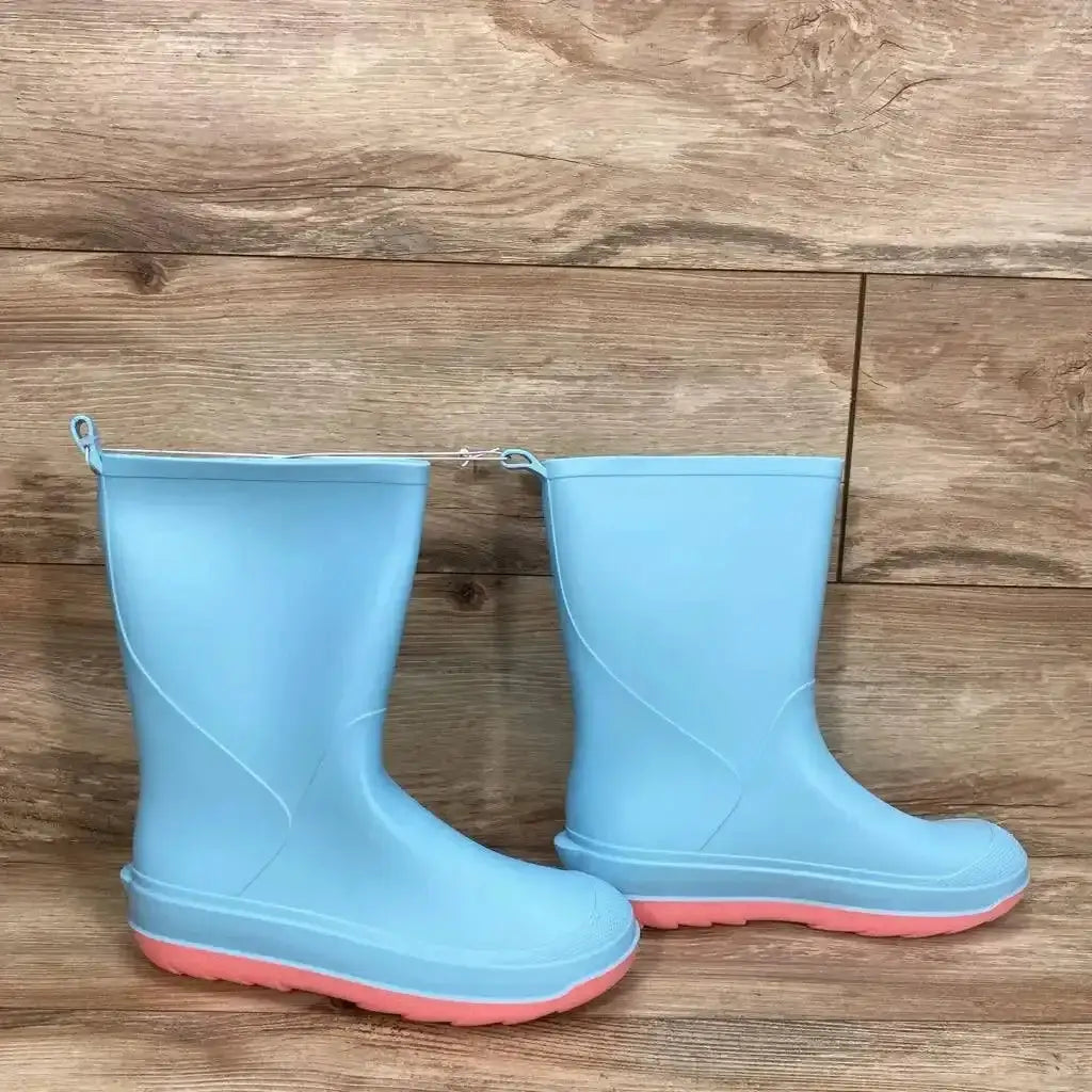 Side view of Cat & Jack children's slip-on rain boots, light blue with pink soles, mid-calf height on wood floor