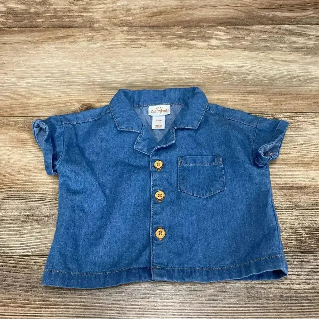 Front view of Cat and Jack chambray baby button-up shirt size 0-3M showing wooden buttons and chest pocket on wood surface