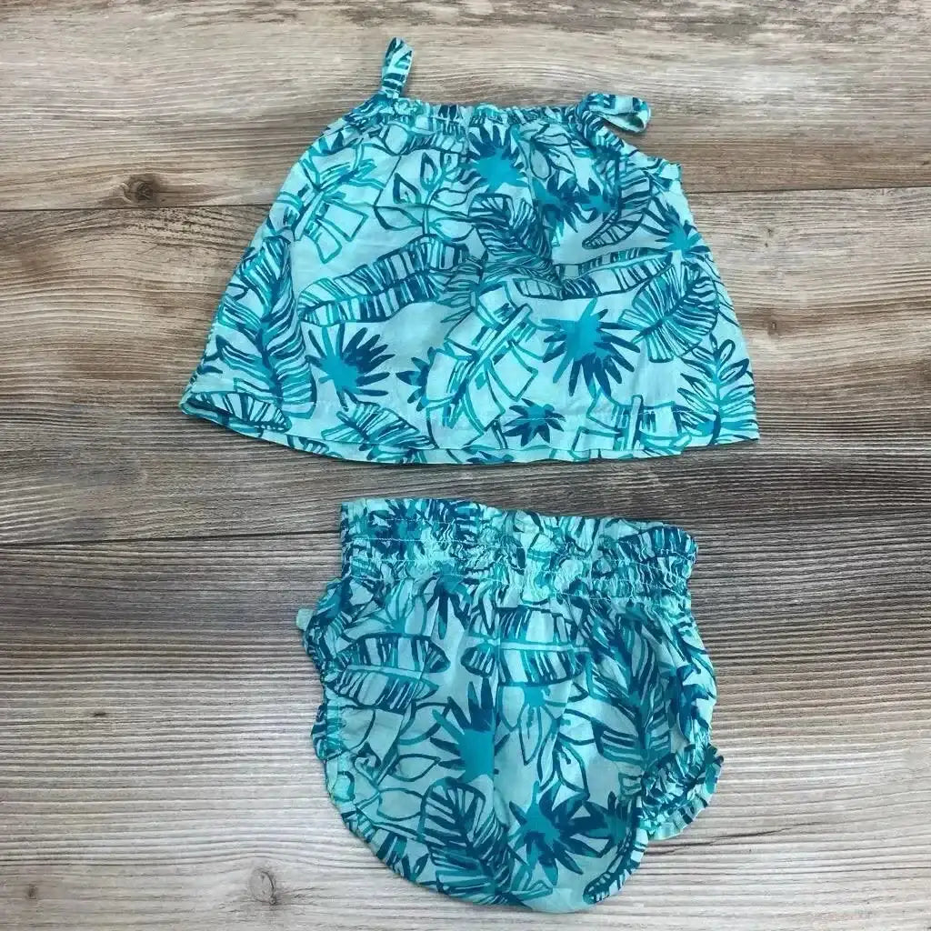 Flat lay of teal tropical two-piece baby top with tie shoulder straps and elastic ruched bloomers on wood background