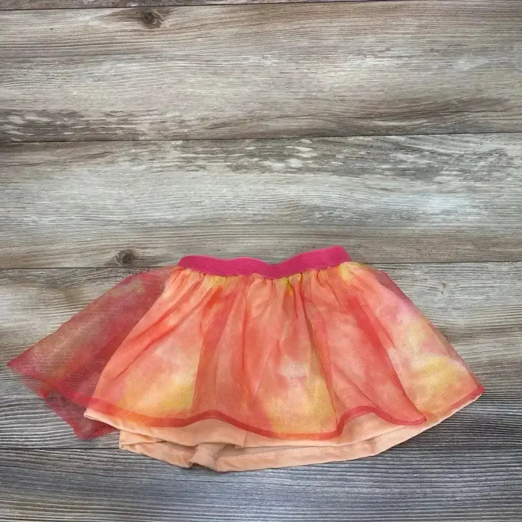 Flat lay of baby tutu skirt, size 12 months, with hot-pink elastic waistband and peach-orange glitter tulle layers on wood background