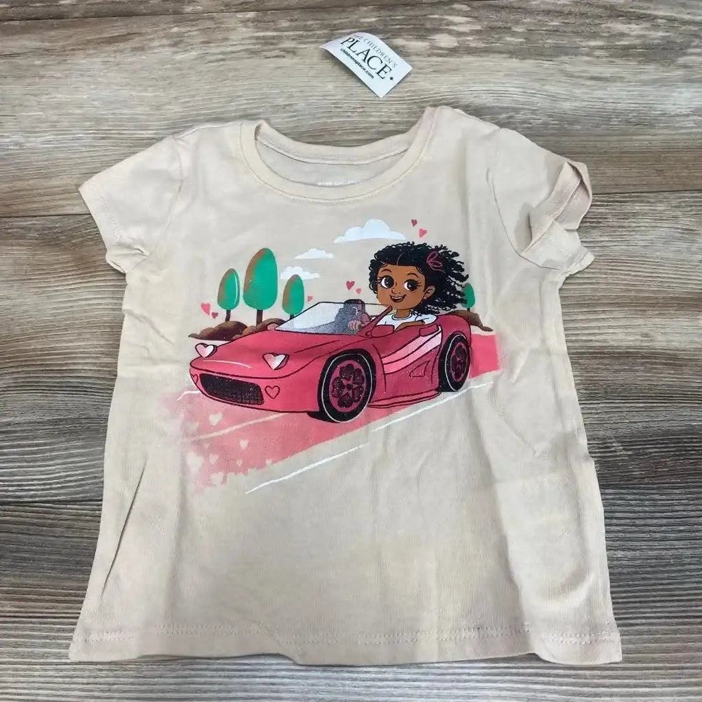 Flat lay of beige Children's Place short-sleeve graphic t-shirt, size 18–24 months, showing pink convertible and girl illustration on wood surface