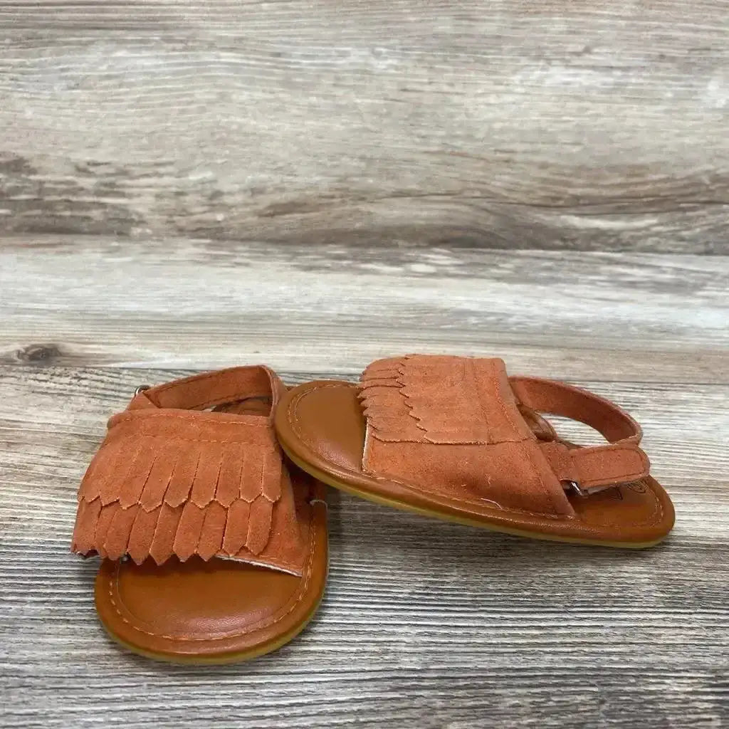 Three-quarter view of toddler Romirus fringe moccasins size 3C showing rust suede fringe and back strap on light wood surface