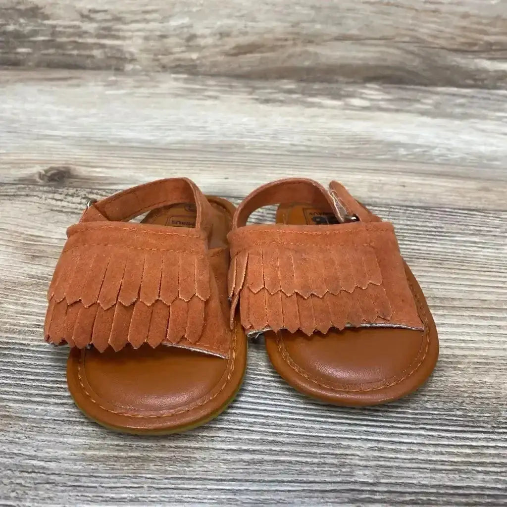 Front view of toddler Romirus fringe moccasins showing brown suede layered fringe over the toes on a wood-grain floor