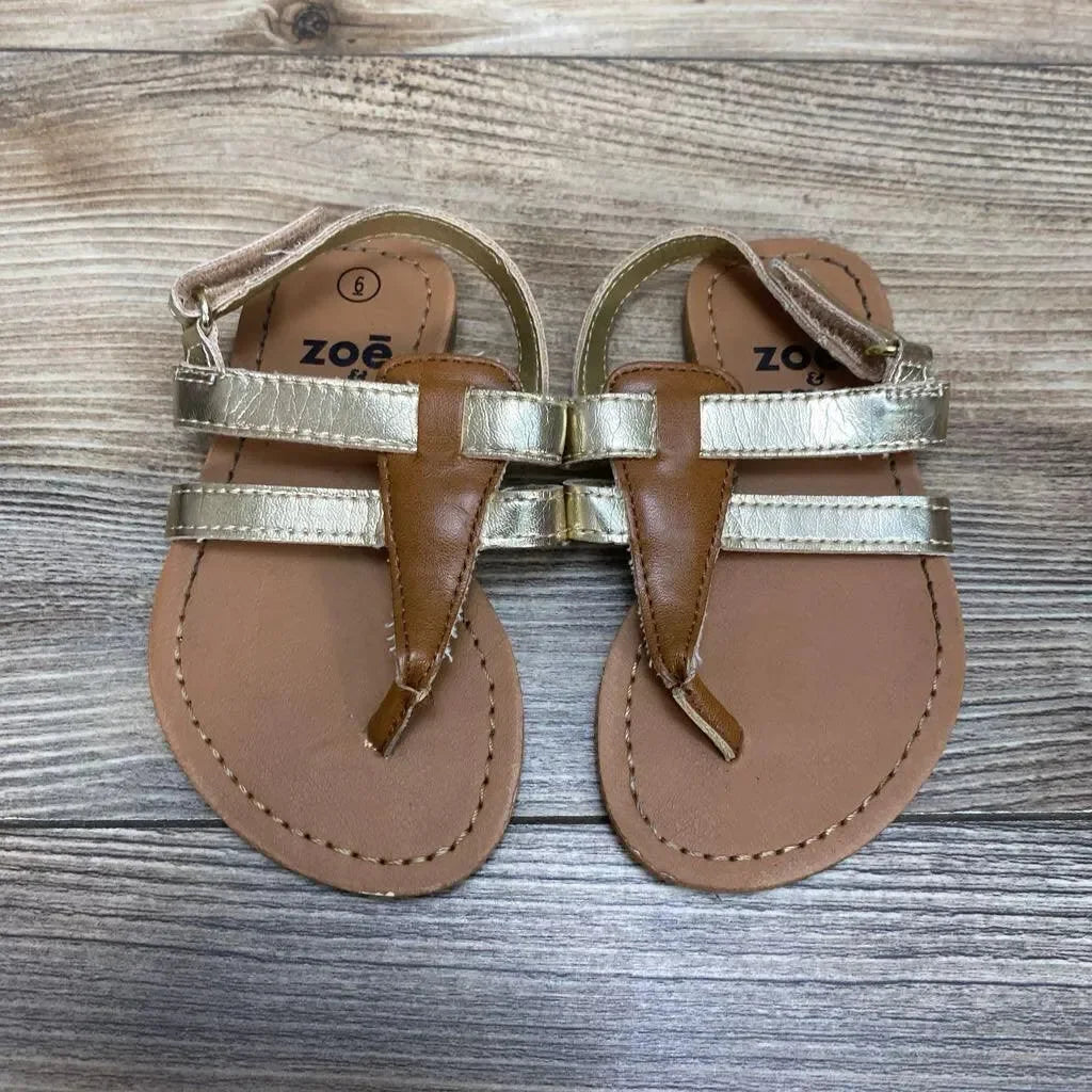 Top view of toddler gold Zoe and Zac sandals size 6C with metallic straps, brown footbed and Velcro ankle strap on wood background