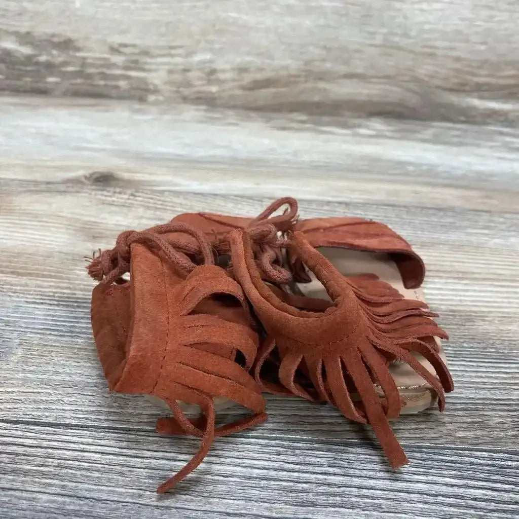 Front-quarter view of red suede Zara baby fringe sandals (size 4C) showcasing fringe and lace ties on light wood background