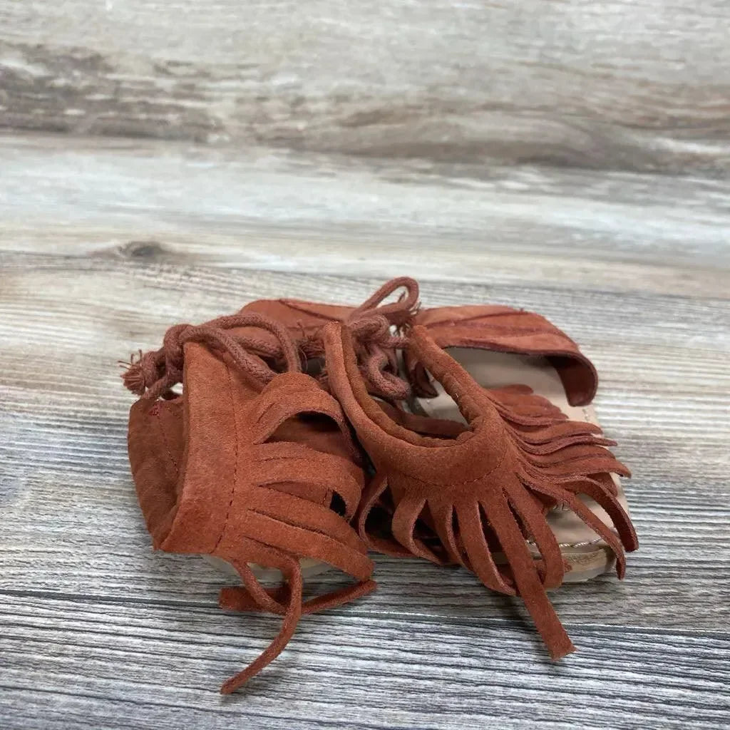 Front-quarter view of red suede Zara baby fringe sandals (size 4C) showcasing fringe and lace ties on light wood background