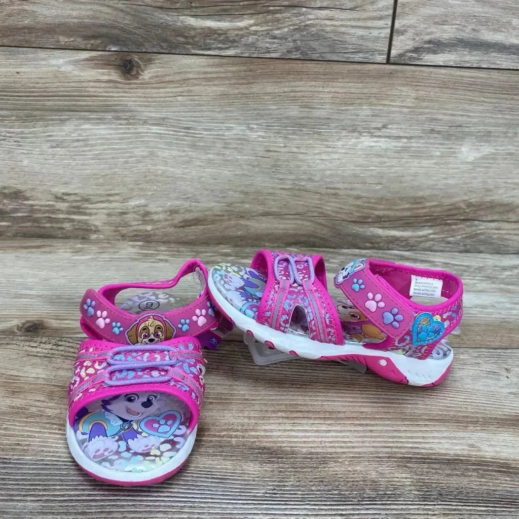 Front and side view of pink Paw Patrol toddler ankle-strap sandals showing character print, double velcro straps and white treaded sole on wood background