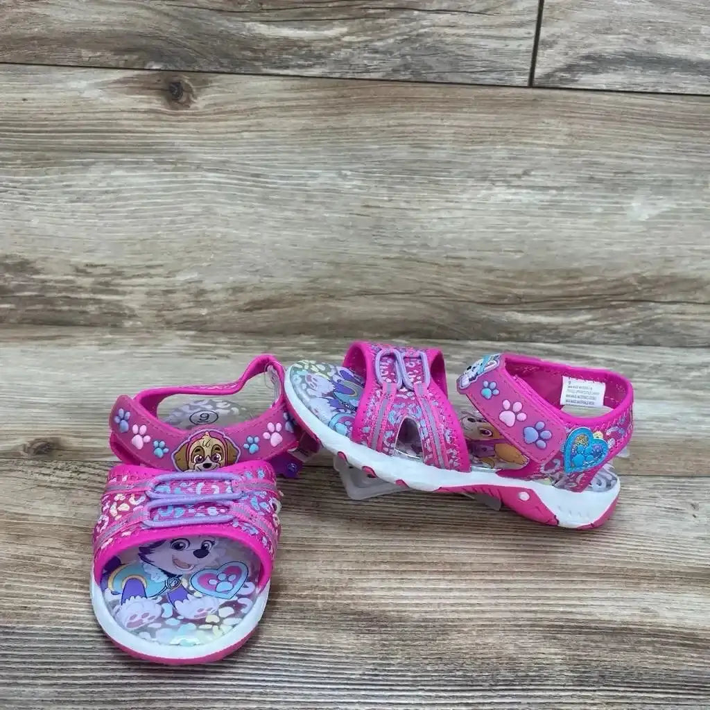 Front and side view of pink Paw Patrol toddler ankle-strap sandals showing character print, double velcro straps and white treaded sole on wood background
