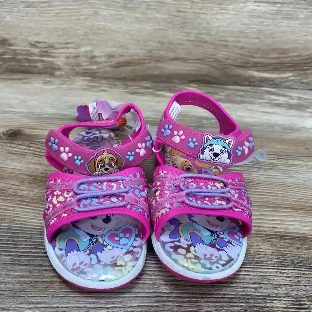 Front view of pink Paw Patrol sandals size 9C with ankle straps, Paw Patrol accents, printed insoles on wood background