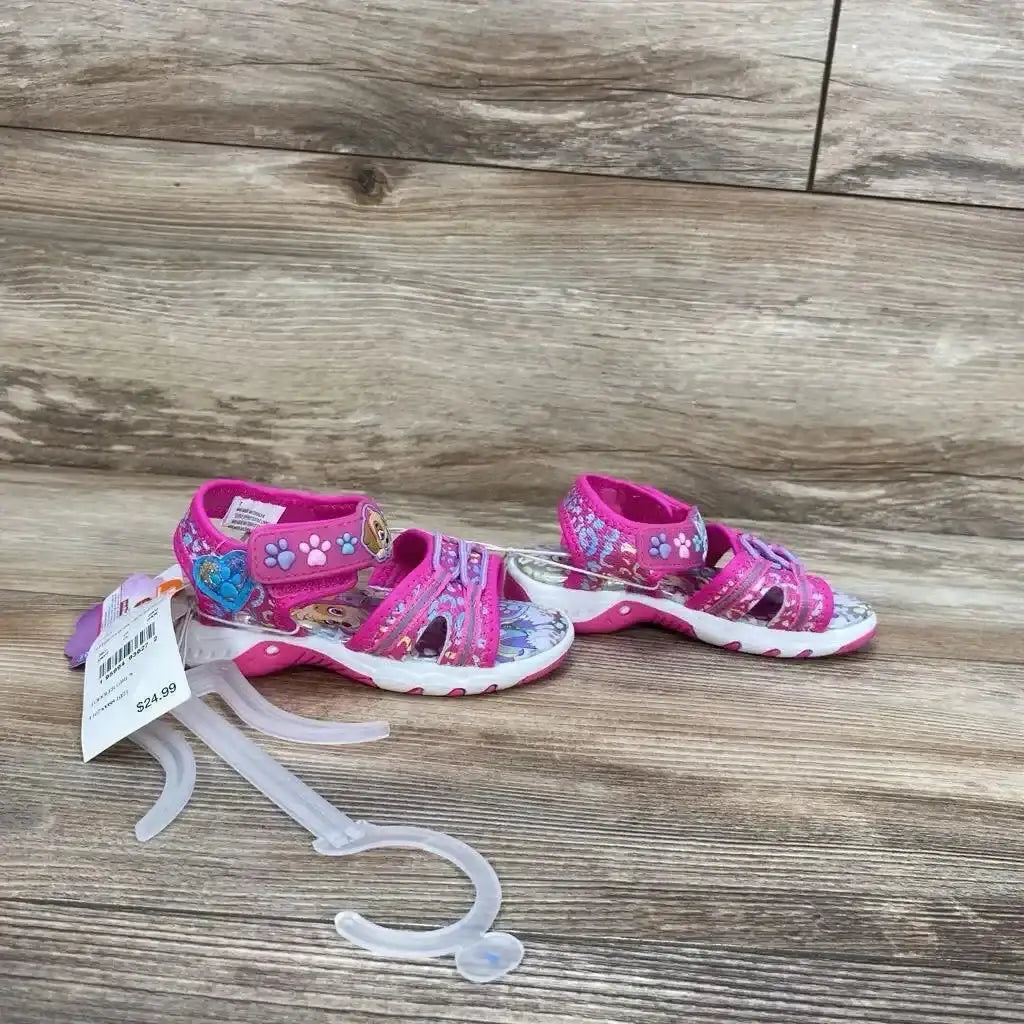 Three-quarter view of NEW Paw Patrol Adventure Ankle Strap Sandals sz 7c in pink with character print and hangtag on wood plank floor