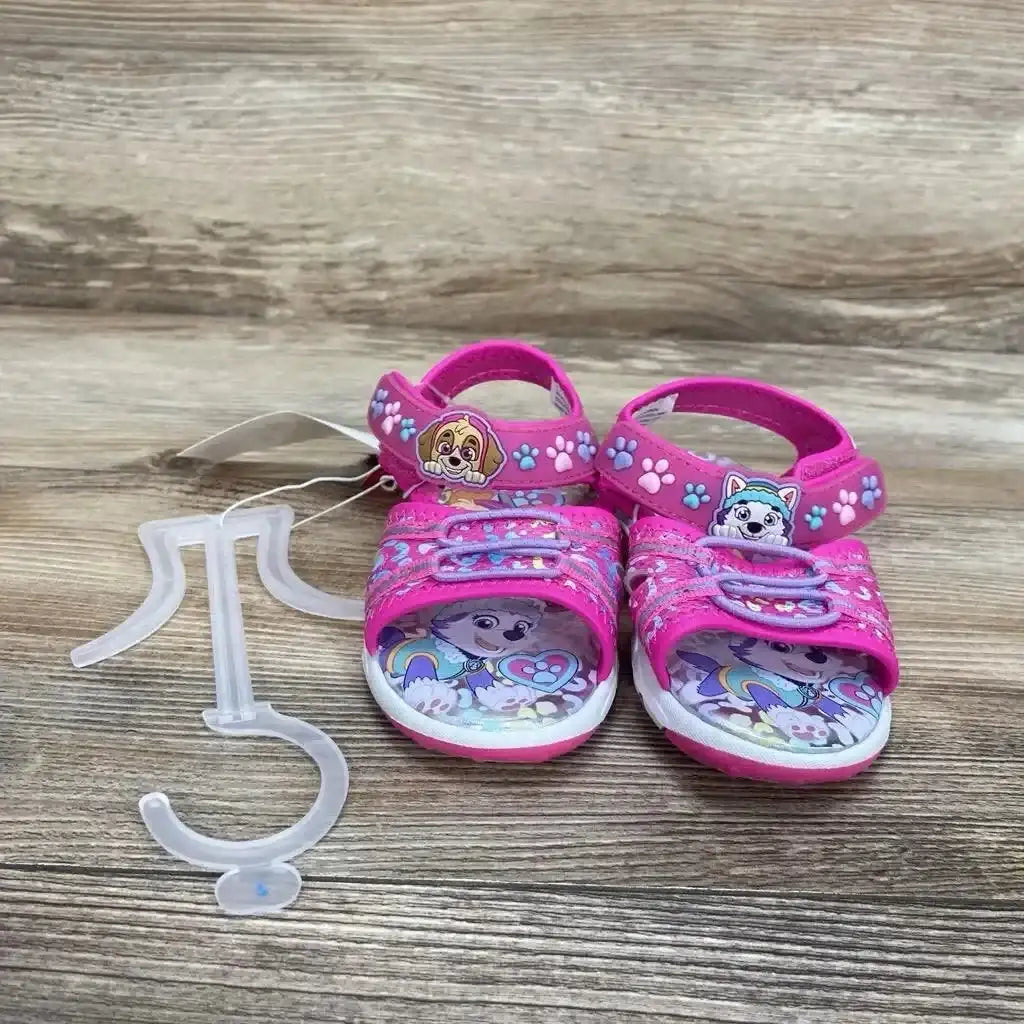 Front view of pink Paw Patrol ankle-strap sandals with character badges, paw-print straps and illustrated insoles